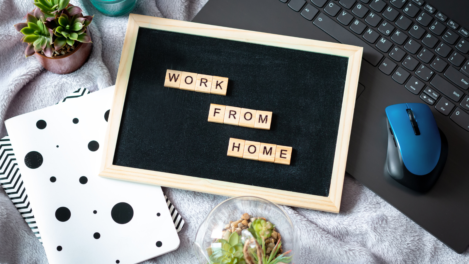 A scrabble board that spells "Work From Home" on top of a laptop and notebook